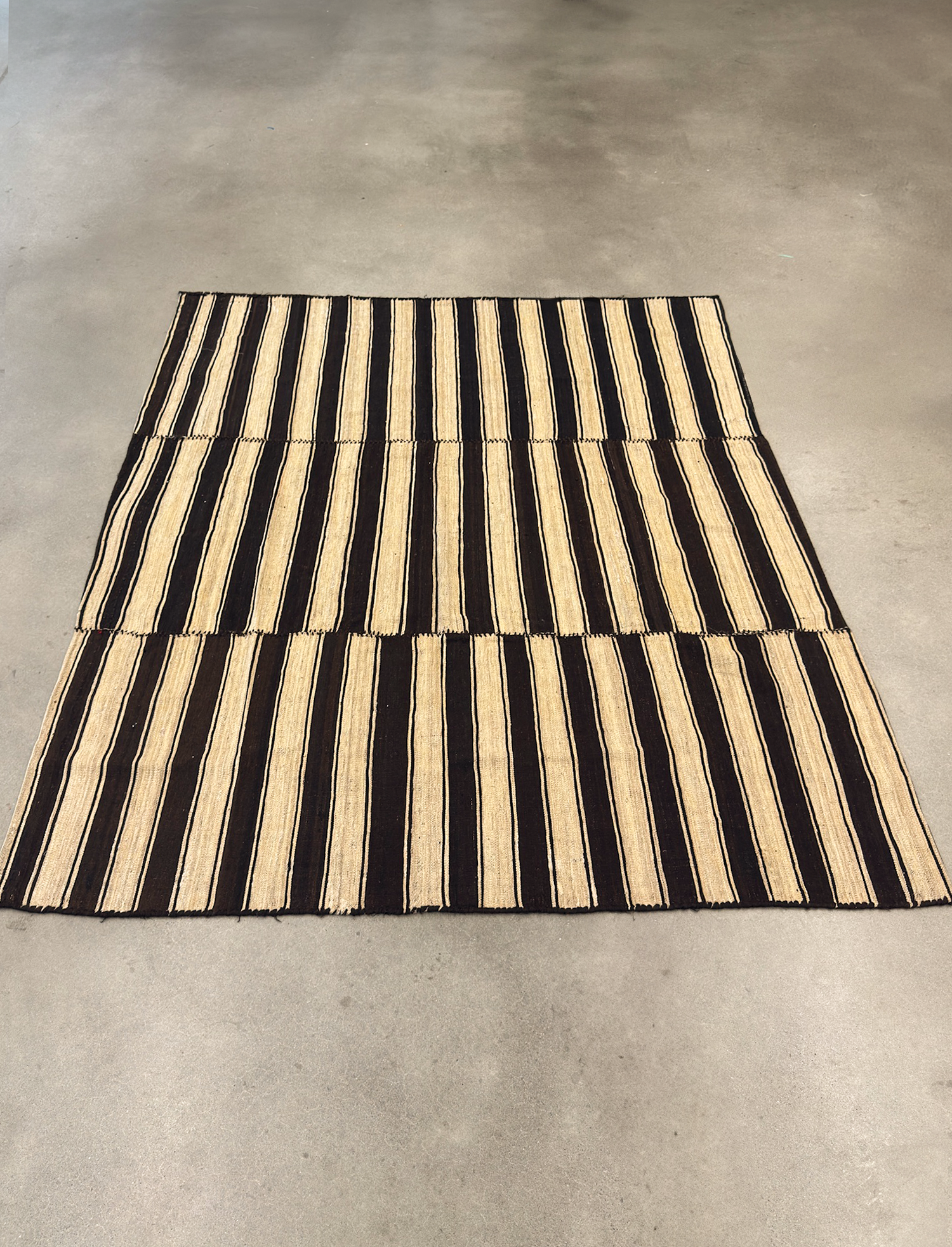 Vintage Iranian Kilim wool rug with a natural beige and brown striped pattern. Handwoven using undyed, raw wool fibers, this one-of-a-kind flatweave textile reflects traditional craftsmanship with a minimal, neutral palette. Its generously scaled 83" × 87" footprint makes it perfect as a centerpiece in living rooms, bedrooms, or creative interiors. The reversible nature and clean-lined geometry make it an ideal choice for mid-century, bohemian, and Japandi-styled spac