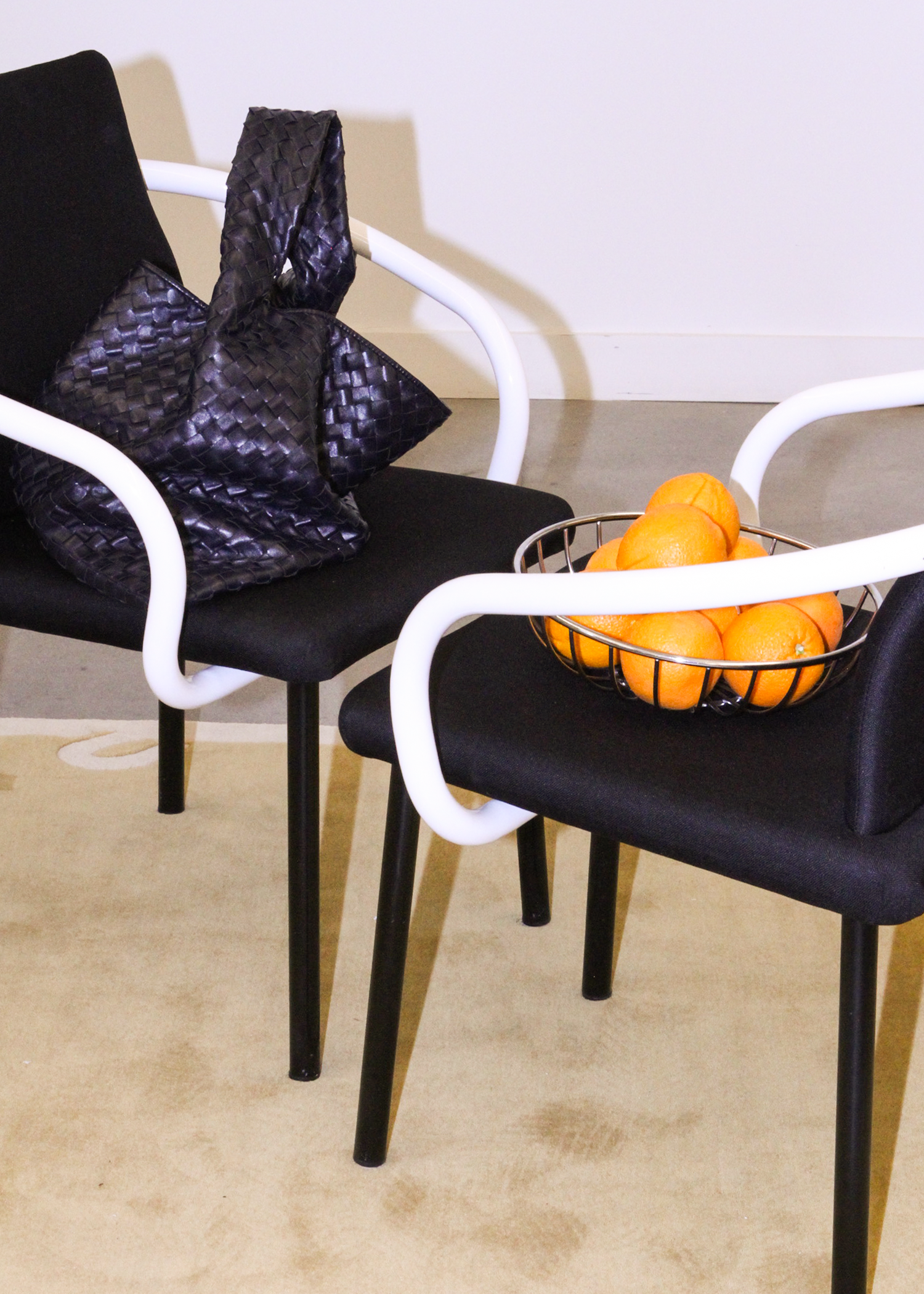 Ettore Sottsass Mandarin Chairs for Knoll, 1986, in black upholstery with sculptural white arms. Italian postmodern design classic styled with a woven leather bag and a wire fruit bowl filled with oranges.